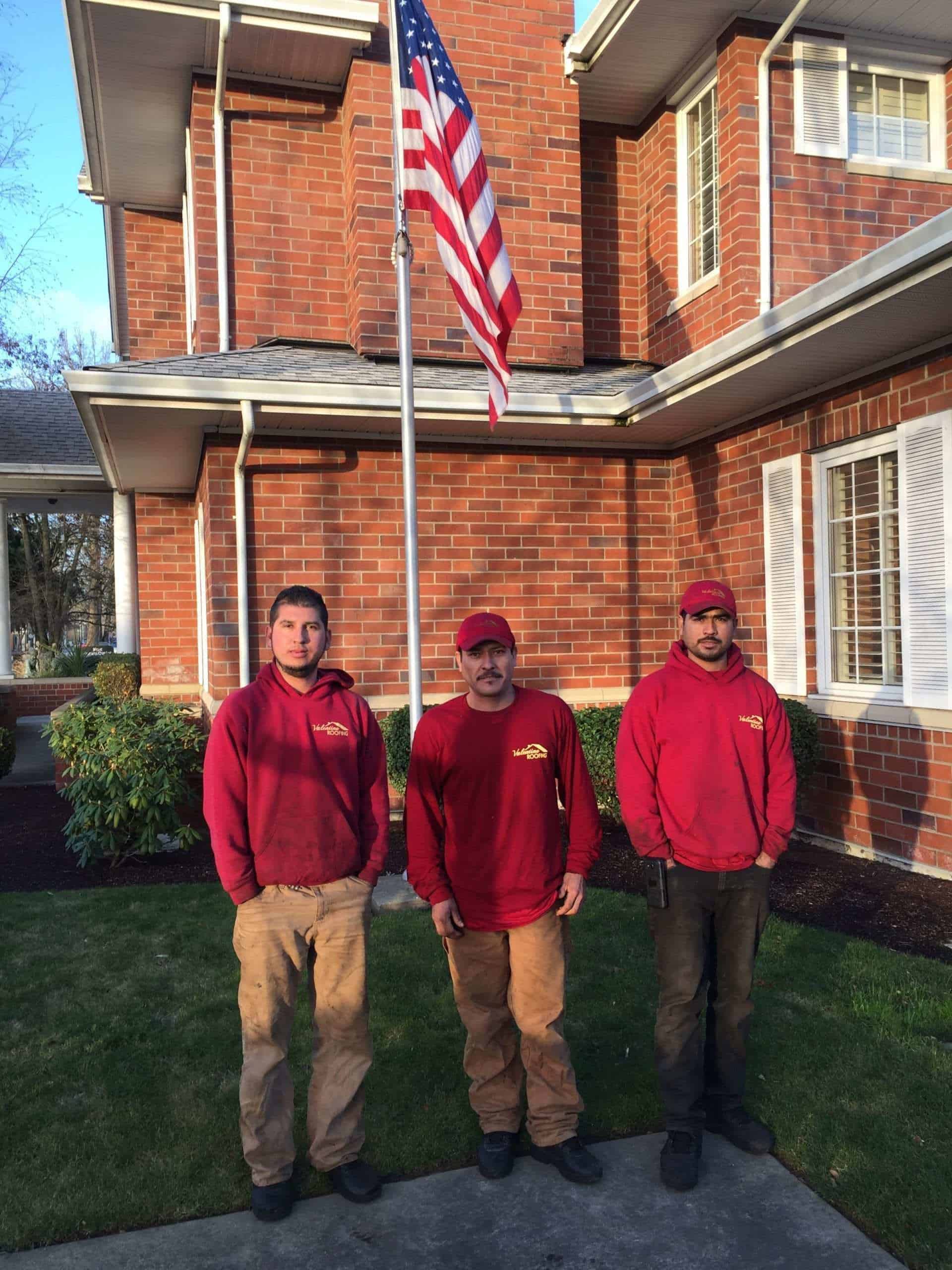 3 male roofers standing under a flag of the United States